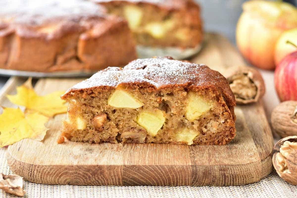 A slice of apple walnut cake on a wooden board.