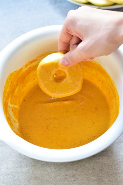 an apple ring is being dunk in pancake batter