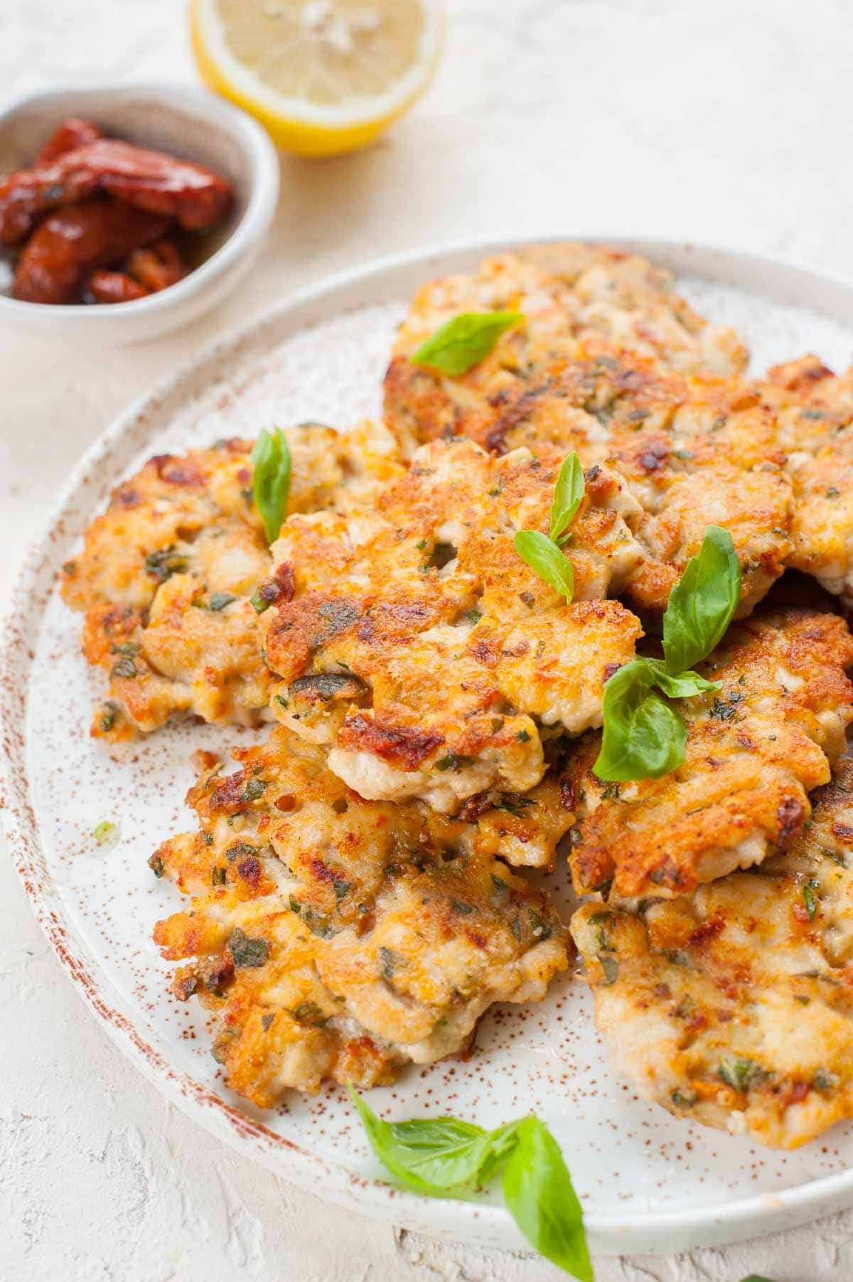 Italian-inspired chicken fritters on a white plate topped with basil leaves.