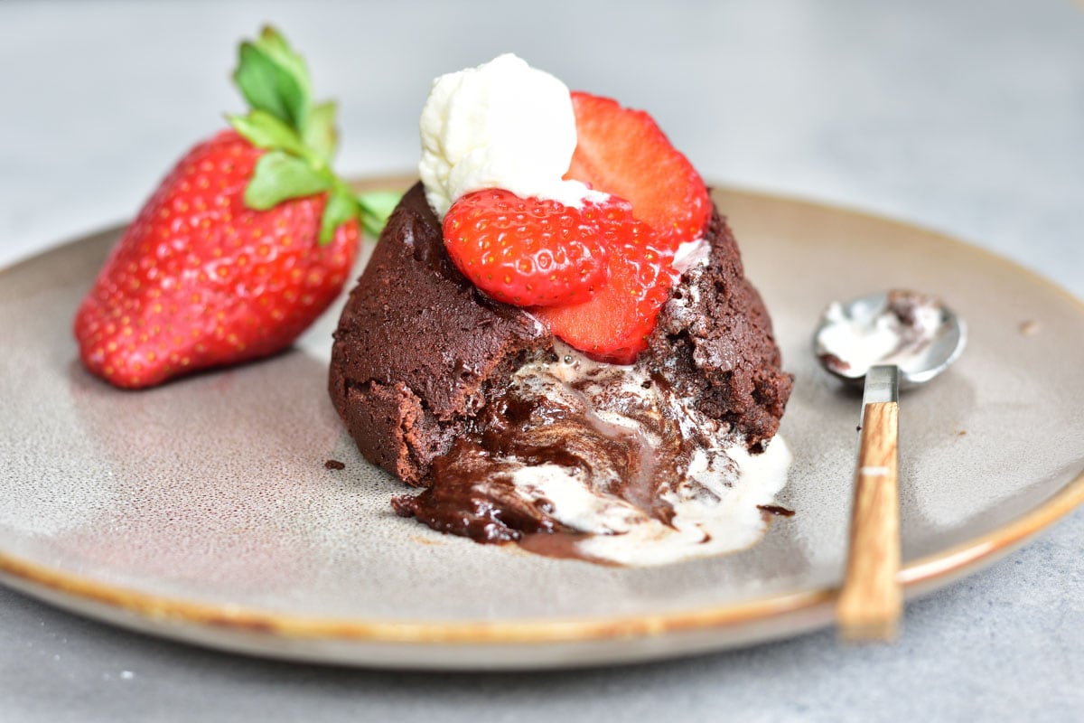 Chocolate lava cake served with whipped cream and strawberries on a plate.