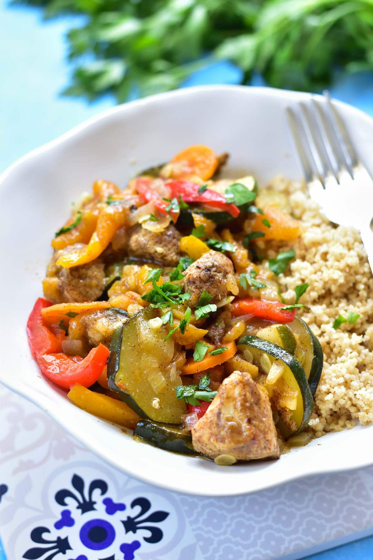 Moroccan chicken with dried apricots and vegetables, served with couscous in a white bowl.
