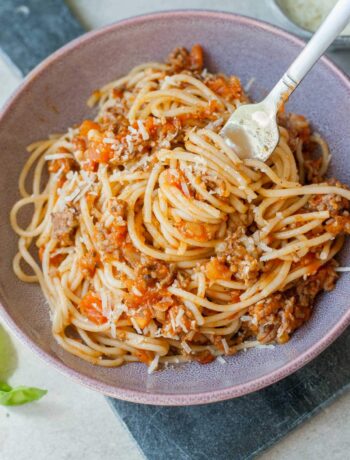 Spaghetti with fresh tomato meat sauce on a fork in a violet bowl.