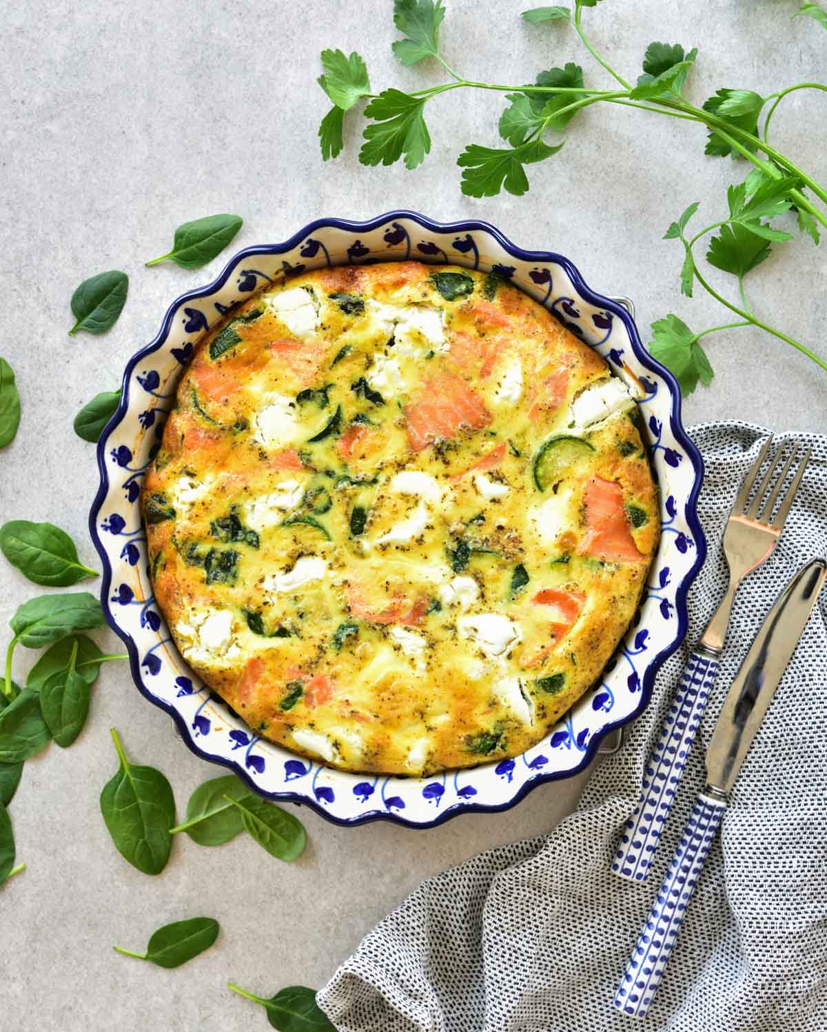 Smoked salmon frittata with zucchini and spinach in a white-blue baking dish.