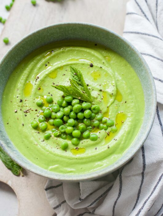 Pea mint puree in a green bowl topped with peas and mint leaves.