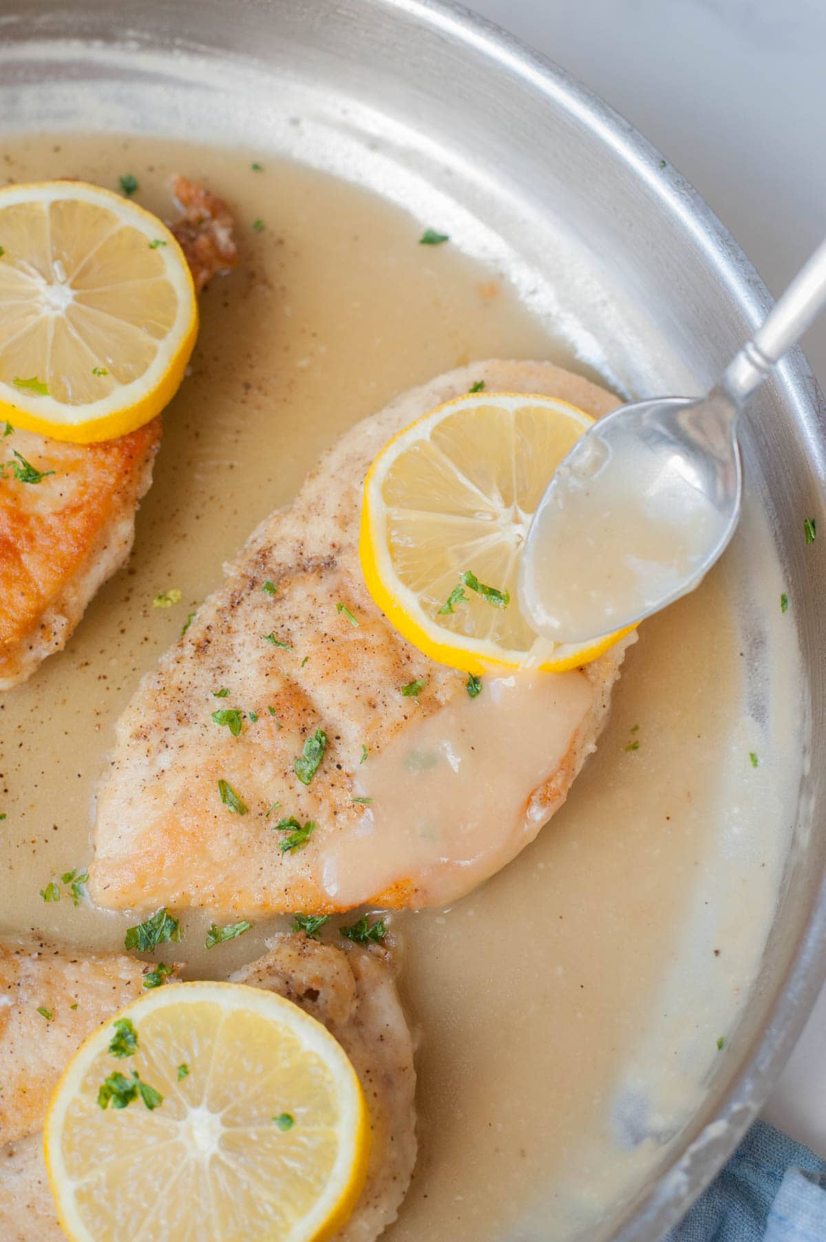 Pan-fried chicken fillet in a frying pan is being poured with lemon butter sauce.