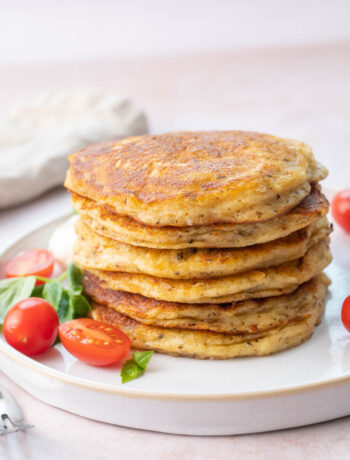 A stack of savory pancakes on a white plate served with tomatoes and basil.