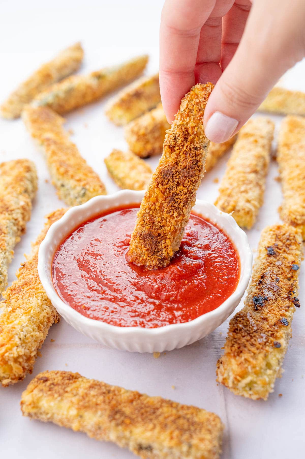 Zucchini fry is being dipped in marinara sauce.