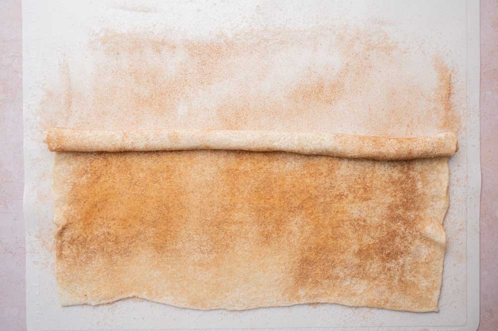 Partially rolled up puff pastry sheet with cinnamon sugar.
