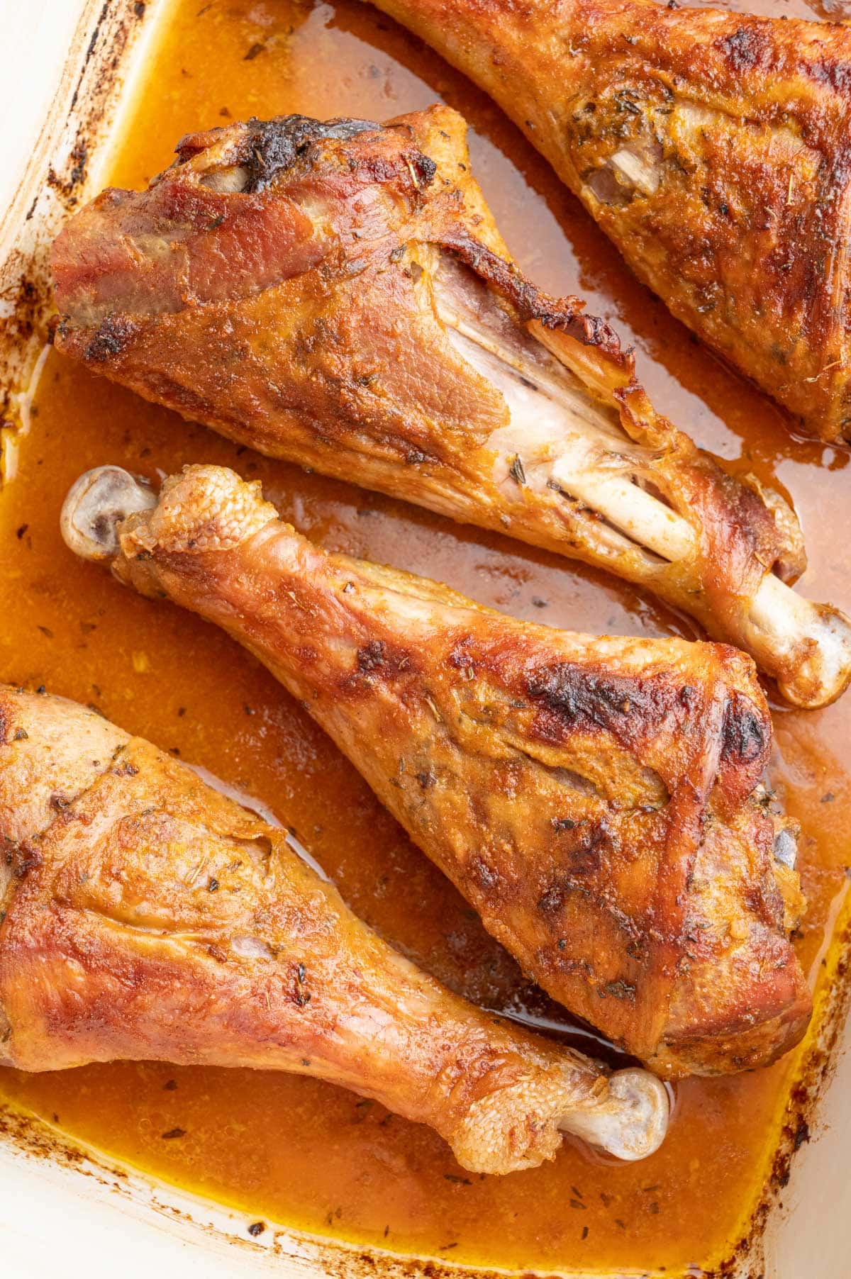 Baked turkey drumsticks in a white baking dish.