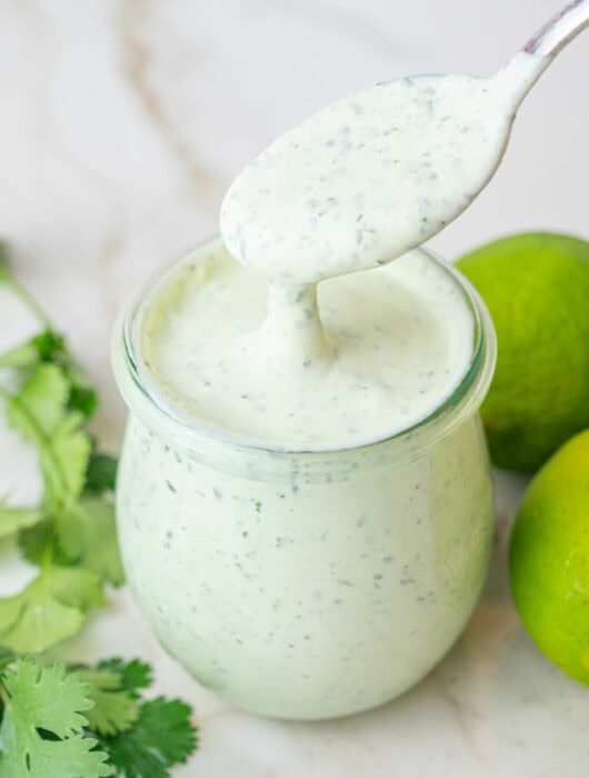Cilantro lime crema in a jar. Cilantro and limes in the background.