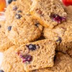 Freshly baked healthy breakfast muffins stacked on a wire cooling rack, with one muffin cut in half to show its soft and moist texture with visible blueberries inside.