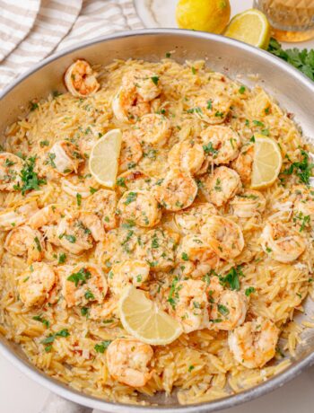 Shrimp scampi orzo served in a large skillet, topped with lemon wedges and chopped parsley, ready to serve.
