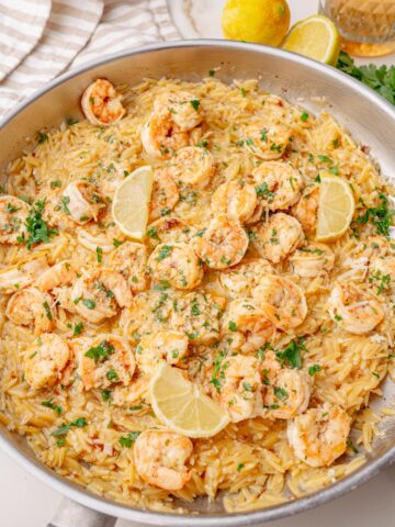 Shrimp scampi orzo served in a large skillet, topped with lemon wedges and chopped parsley, ready to serve.