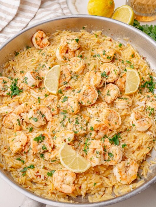Shrimp scampi orzo served in a large skillet, topped with lemon wedges and chopped parsley, ready to serve.