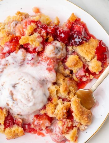 Close-up of a serving of strawberry rhubarb crumble on a plate with melted ice cream and a spoon.