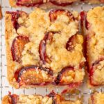 Close-up of a slice of German plum cake with a buttery crumb topping and baked plum halves, showing crisp edges and juicy fruit.