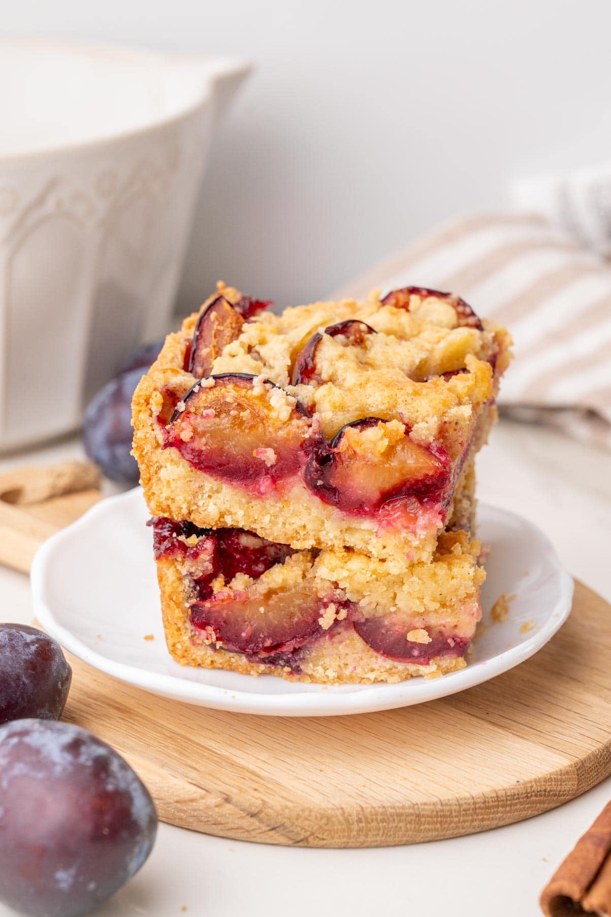 Two stacked slices of German plum cake on a white plate, revealing layers of golden crumb, juicy plums, and a shortcrust base.