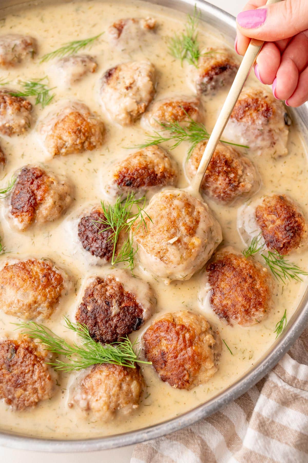 A close up photo of Polish meatballs with dill sauce in a frying pan.