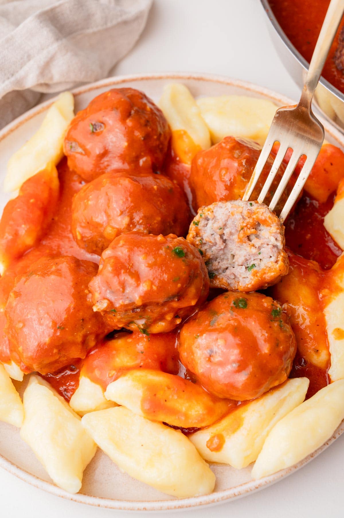 Meatballs with tomato sauce served with kopytka dumplings on a white plate.