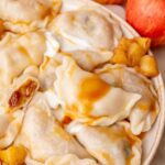 Apple pierogi on a beige plate served with caramel sauce and sour cream.