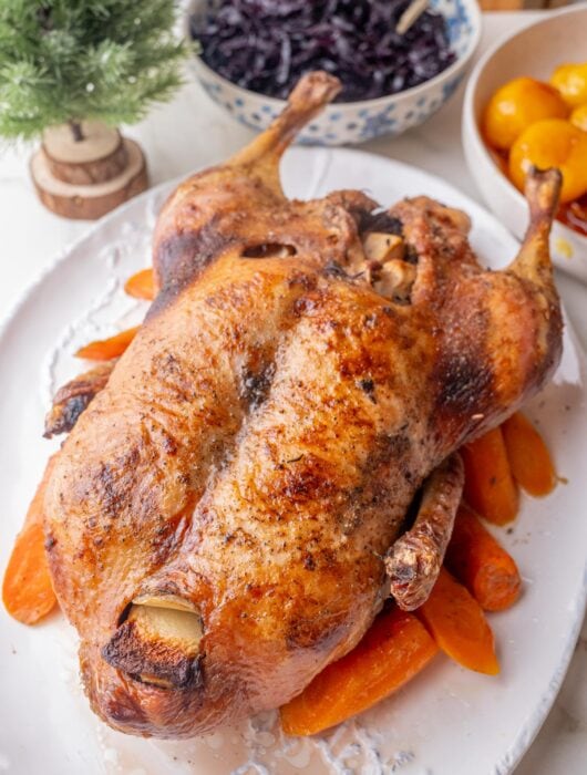 Danish Christmas Duck on a white plate with caramel potatoes and red cabbage in the background.