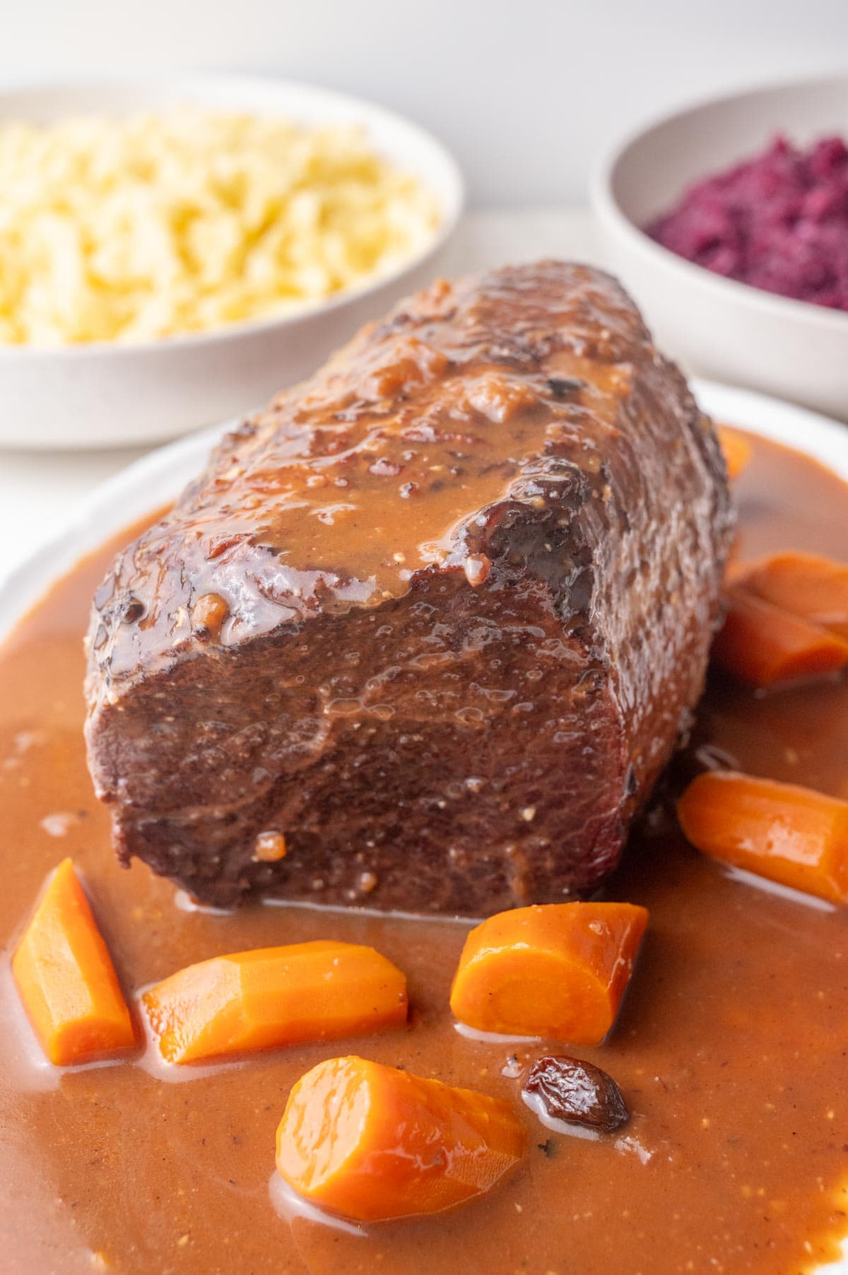 Sauerbraten roast with gingerbread sauce and carrots on a white plate.